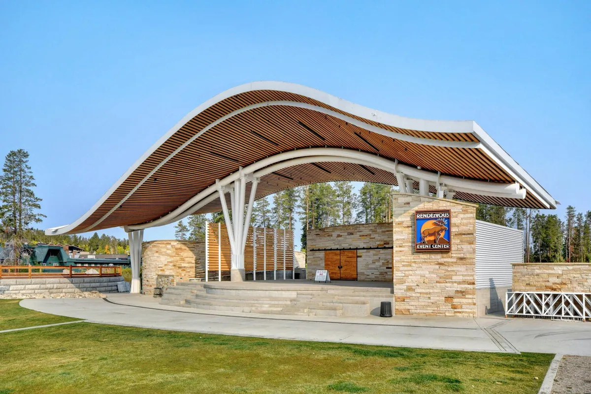 This exterior image showcases the Hideaway Park amphitheater, a unique curved roof structure surrounded by stone walls and community signage, set in an inviting outdoor area perfect for concerts and family gatherings.