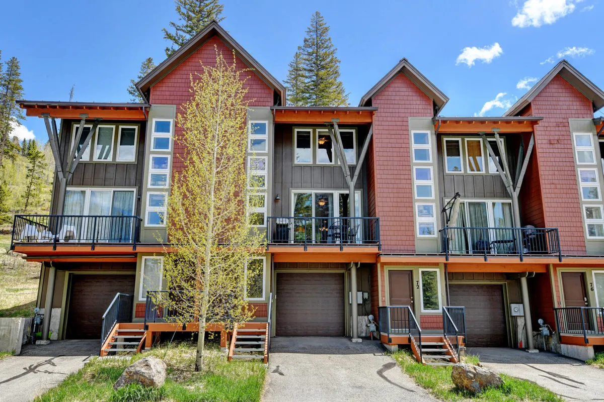 The image showcases the striking exterior of a contemporary mountain chalet, with sleek architecture framed by mature trees. Expansive balconies with glass railings invite relaxation, offering sweeping views of the surrounding Colorado wilderness. The setting feels peaceful and sunlit, perfect for both morning coffee and stargazing nights.
