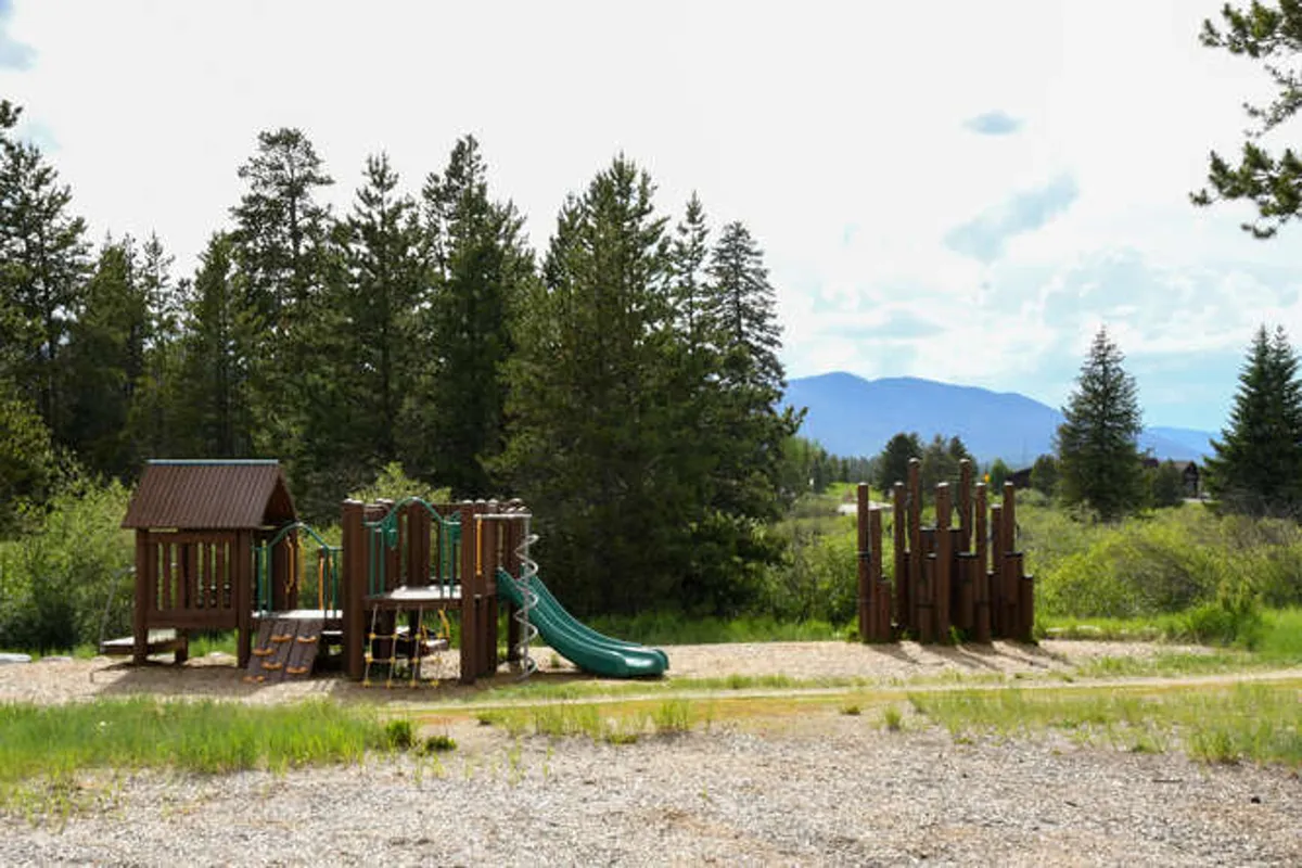 A vibrant playground set against a backdrop of trees, featuring green slides, a wooden playhouse, and open spaces for families or kids to play and gather.