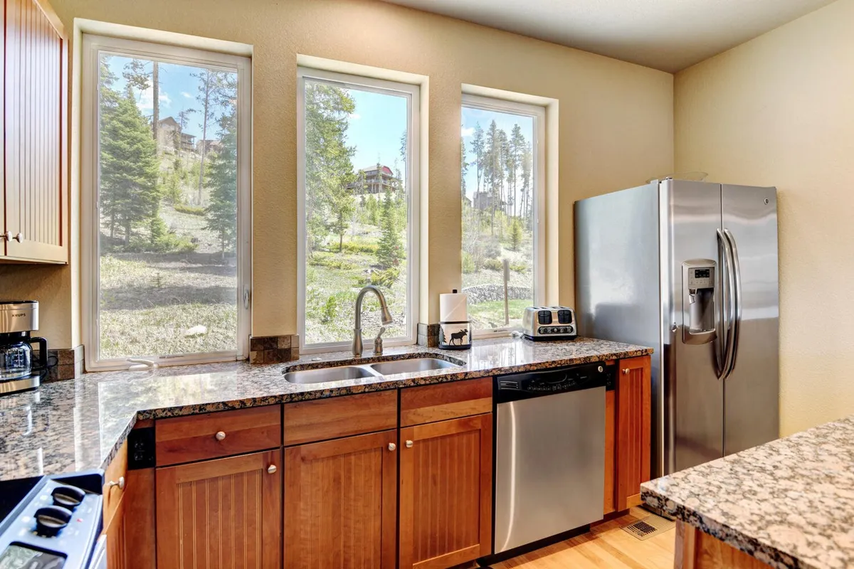 A bright, welcoming kitchen with granite countertops, stainless steel appliances, and large windows offering beautiful views. The atmosphere encourages both cooking and casual breakfasts, with room for multiple people to gather and enjoy the space together.