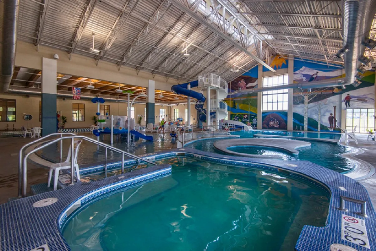 A vibrant indoor pool area with colorful water slides and children playing joyfully among murals, capturing the fun and energy of a family water adventure.