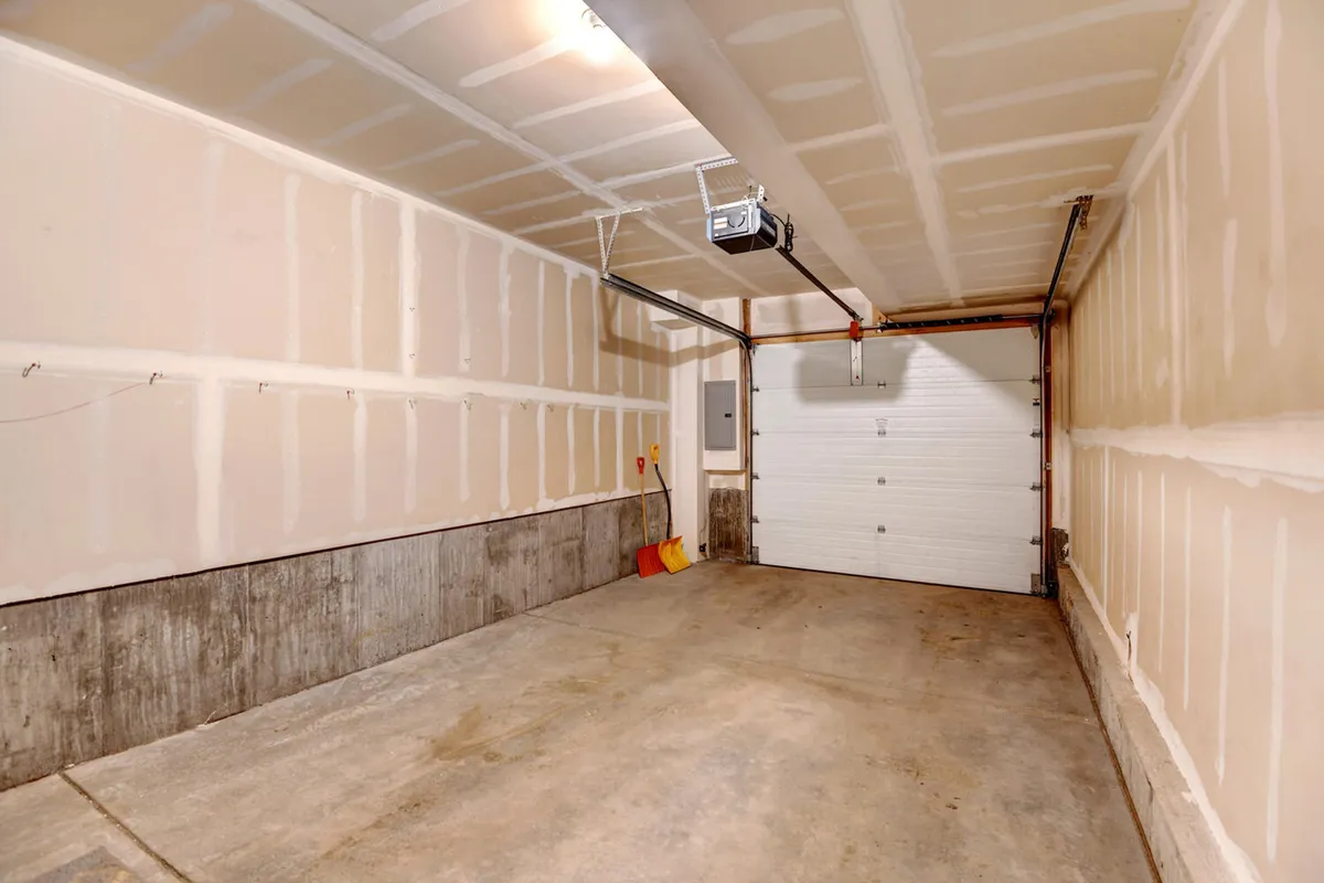 A view inside a spacious garage with clean walls, lighting fixtures, and a large garage door, evoking ample room for storing outdoor gear like skis, bikes, or snowboards. The space is uncluttered and functional.