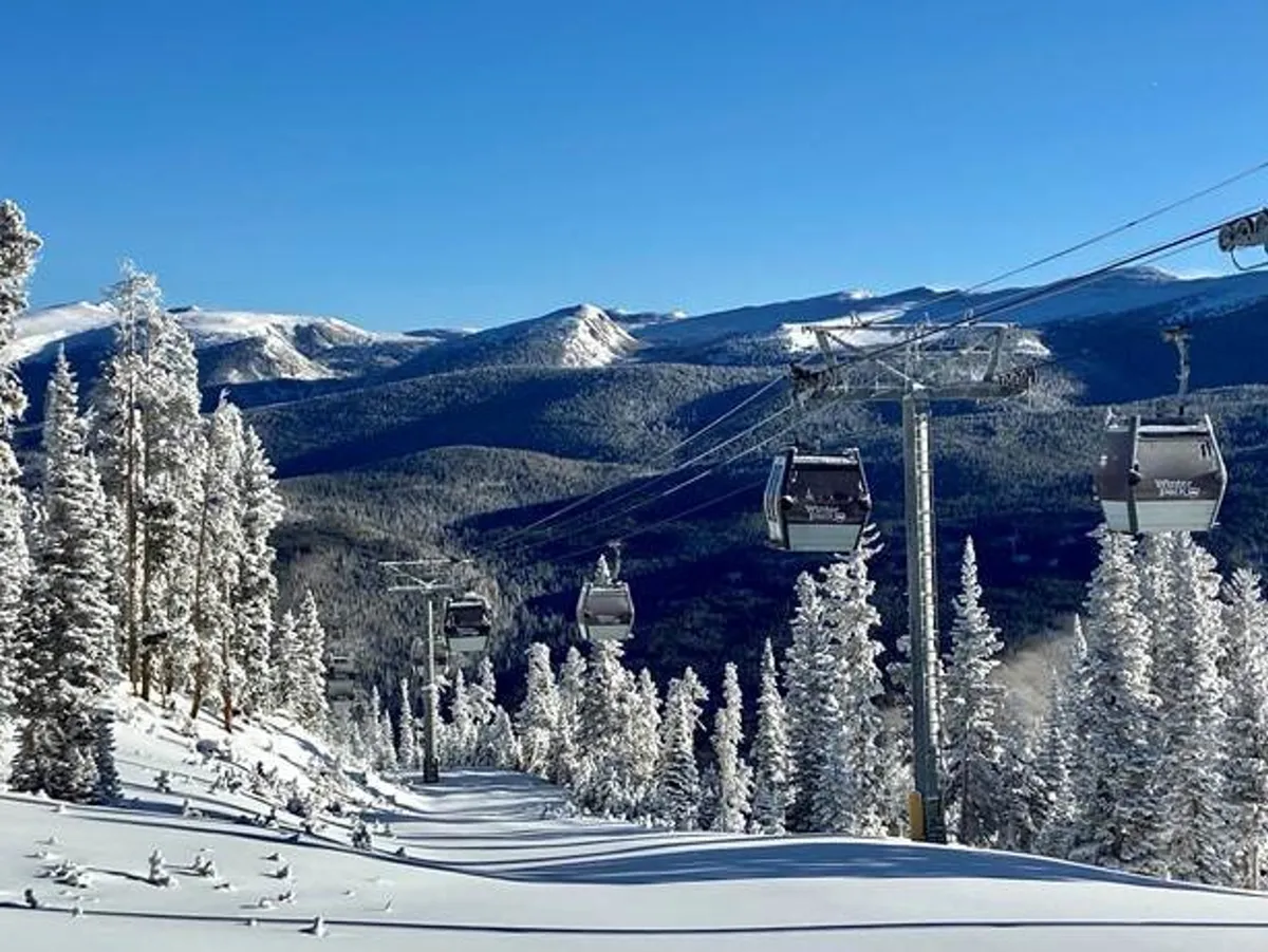This exterior image showcases ski lift gondolas gliding over snow-laden trees with dramatic mountain peaks in the background. The scene embodies the spirit of adventure and all-season activities available right outside the chalet.